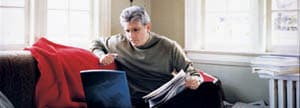 Man sitting on a couch with a laptop and newspaper